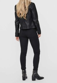 Giacca di pelle nera abbinata a pantaloni neri aderenti e stivaletti. La giacca ha una lunghezza corta e una texture liscia, mentre i pantaloni sono eleganti.