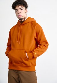 Orange hooded sweatshirt with a front pocket, ribbed cuffs, and a yellow logo accent on the left sleeve. Soft, textured fabric.