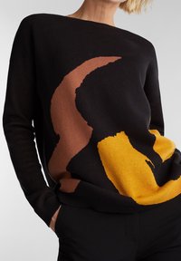 Svart tröja med abstrakta mönster i brunt och gult. Har en bred halsringning och långa ärmar, tillverkad i mjukt stickat material.