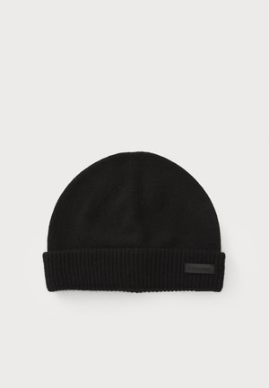 Bonnet en tricot noir avec un revers côtelé et un dessus plat. Fabriqué en tissu doux, il présente une petite étiquette sur le revers.