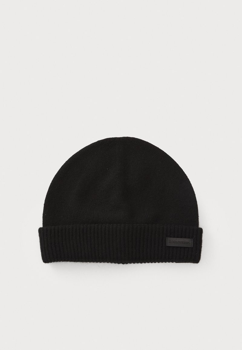 Black knitted beanie hat with a ribbed cuff and a flat top. Made from soft fabric, features a small label on the cuff.