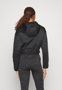 Felpa nera tagliata con una texture liscia, dotata di un grande cappuccio e orlo a coste, abbinata a leggings neri con un motivo a vortice.