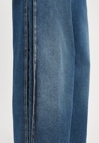 Denim jeans in medium blue, featuring a straight leg design, contrast stitching, and a smooth texture with faint whiskering details.