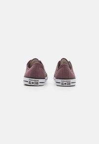 Burgundia kangastossud madala disainiga, valged kummitaldad ja must "Converse All Star" bränding kanna peal.