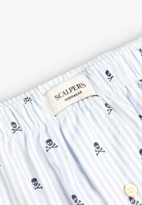 Boxers de algodón en azul claro con rayas blancas, con patrones de calaveras y tibias en negro, la etiqueta de la cinturilla dice "SCALPERS UNDERWEAR".
