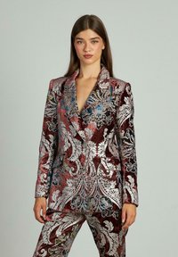 Traje de terciopelo en burdeos con intrincados patrones florales en plata y azul, que cuenta con un cuello de muesca, botones dobles y bolsillos frontales.