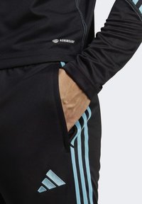 Černé sportovní kalhoty s světle modrými bočními pruhy, vyrobené z materiálu odvádějícího vlhkost, s označením AeroReady na pase.