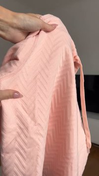 Tissu rose texturé avec un motif en chevrons. Le pull a une encolure ronde et est tenu avec une main.