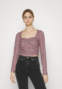 Top cropped de manga longa com padrão de onça rosa, com decote quadrado, detalhe franzido na frente e tecido texturizado, combinado com jeans pretos de cintura alta.