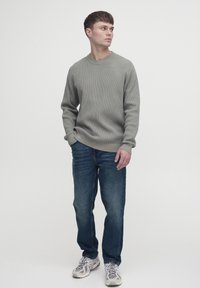 Pulover gri cu manșete rib, cu guler rotund, asociat cu blugi de culoare albastru închis și adidași de culori deschise. Design simplu și casual.