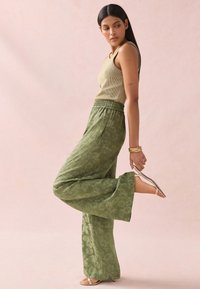 Pantalon large couleur olive avec un motif floral, taille élastique, associé à un débardeur côtelé beige et des sandales à brides.