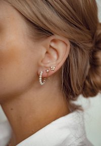 Boucle d'oreille en or avec des accents de perles, accompagnée d'un clou de fleur avec des détails en perles. Texture lisse, éclat subtil et design délicat.