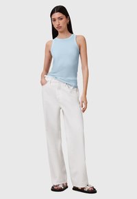 Světle modrý přiléhavý top s ramínky, kombinovaný s bílými volnými kalhotami. Oblečení má jednoduchý design a hladké textury látky.