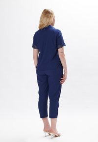 Completo due pezzi blu navy composto da una maglietta a maniche corte con dettagli in rete e pantaloni cropped. Realizzato in un tessuto leggero.