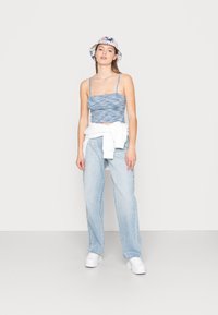 Top cropped azul texturizado com alças finas, emparelhado com jeans de lavagem clara e ténis brancos. Um chapéu tipo balde com padrão floral completa o visual.