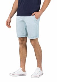 Hellblaue Baumwollshorts mit umgeschlagenen Säumen, Seitentaschen und einem braunen Knopfdetail, kombiniert mit weißen Sneakers.