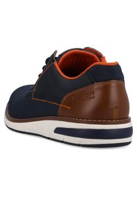 Marineblauer Sneaker mit braunen Lederakzenten, textured Stoffoberfläche, orangefarbener Polsterung und weißer Sohle mit marineblauem Streifen. RIEKER-Branding an der Ferse.