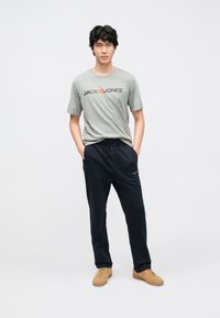 Grå bomulls t-skjorte med «JACK & JONES»-logo; mørkeblå joggebukser med elastisk midjebånd; beige sneakers med teksturert overflate.