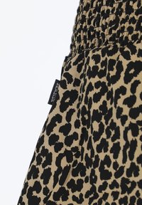 Leopardmønstret stof i tan og sort med en smocket talje. En label med teksten "SEASIDE" er synlig på stoffets kant.