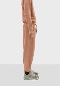 Peach-colored sweat top and joggers made from soft fabric, featuring an elastic waistband and cuffed ankles; gray athletic shoes with accents.
