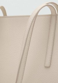 Bolso tote de cuero color beige con acabado texturizado, que presenta dos asas delgadas y detalles de costura visibles a lo largo de los bordes.