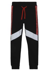 Černé tepláky s bílými diagonálními pruhy a červeným nápisem "GUESS" na boku. Mají elastický pas s červeným šňůrkem.