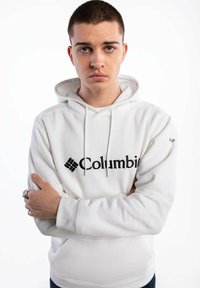 Biała bluza z kapturem z czarnym logo „Columbia” na przodzie, z kieszenią kangurzą i sznurkami przy dekolcie.