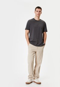 Camiseta gris de manga corta combinada con pantalones beige y zapatillas blancas con suelas marrones. La tela parece suave y cómoda.