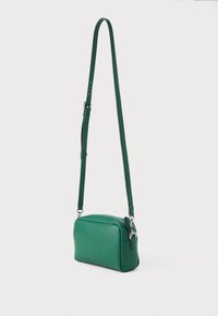 Πράσινη δερμάτινη τσάντα χιαστί με λεία υφή, ορθογώνιο σχήμα, ρυθμιζόμενο λουρί και ασημένια εξαρτήματα.