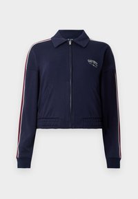 Navy blue cropped jacket made of soft fabric, featuring a zip closure, collar, and contrasting red and white stripes along the sleeves.
