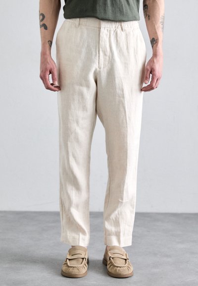 Pantalons en lin de couleur beige clair avec une coupe décontractée, dotés d'une taille ajustable avec cordon et de poches latérales, associés à des chaussures beiges à enfiler.