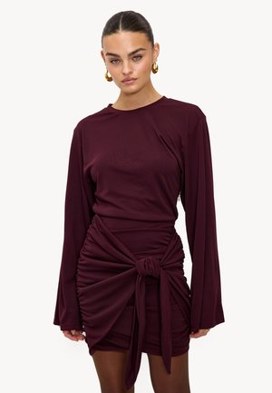 Robe bordeaux à manches longues avec un détail noué à la taille et une texture froncée. Tissu lisse, coupe ajustée avec un col rond.