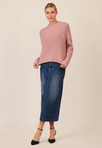 Pink knitted sweater with a textured pattern, paired with a blue denim skirt featuring a dotted design, complemented by black heeled shoes.