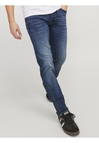 Mörkblå denimjeans med rak passform, lätt blekning på låren och kontrasterande sömmar. Kombineras med svarta sportskor.