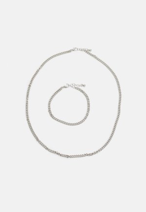 Conjunto de colar e pulseira em prata; apresenta elos entrelaçados com uma textura suave. Ambos têm um fecho em lagosta para ajuste.