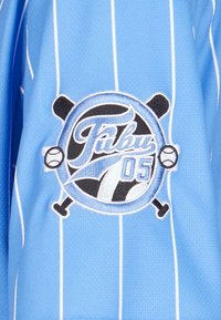 Tricou de baseball de culoare albastră deschisă cu dungi albe, având un logo circular brodat, "Tibuy 05," cu băie de baseball încrucișate.