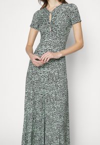 Maxi dress in black and light green, featuring a v-neck, short sleeves, and a gathered detail with a keyhole opening at the front.