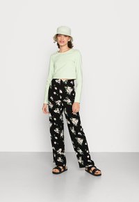 Top cropped de manga longa verde-claro combinado com calças largas pretas com padrão floral e sandálias de plataforma pretas. O chap�éu é de estilo balde verde-claro.