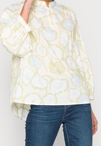 Blouse ample à manches longues en tissu léger, présentant un motif floral jaune et bleu clair avec un colmandarin.