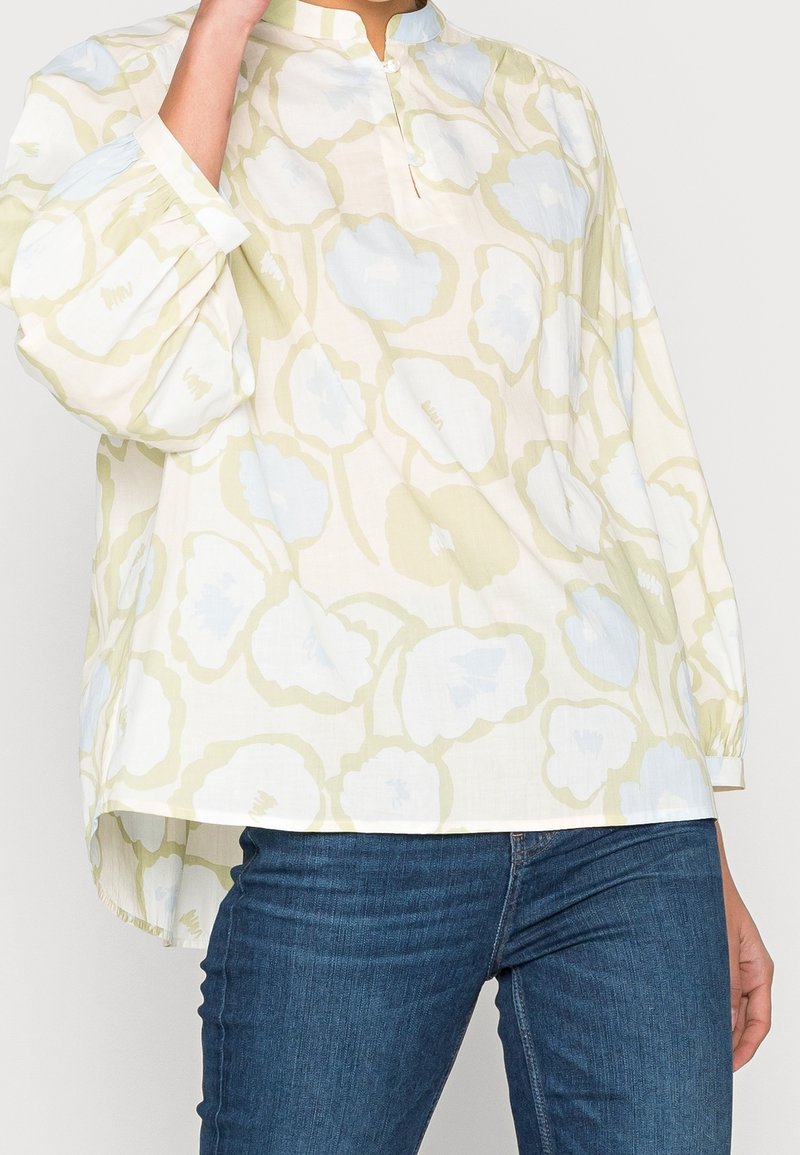 Blouse ample à manches longues en tissu léger, présentant un motif floral jaune et bleu clair avec un colmandarin.