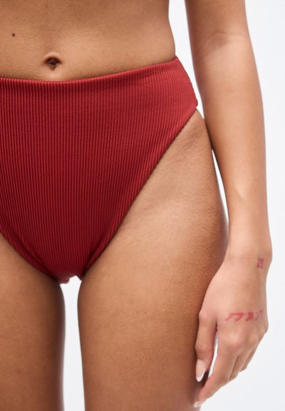 Μπικίνι σλιπ με ψηλή μέση, ριμπ ύφασμα σε βαθύ κόκκινο χρώμα με ομαλή υφή και καθαρές γραμμές, με ανοίγματα ποδιών σε ψηλή κοπή.