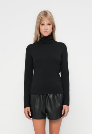 Langermet svart genser med høy hals laget av myk fabric, tettsittende design; kombinert med svarte faux skinnshorts, glatt tekstur.