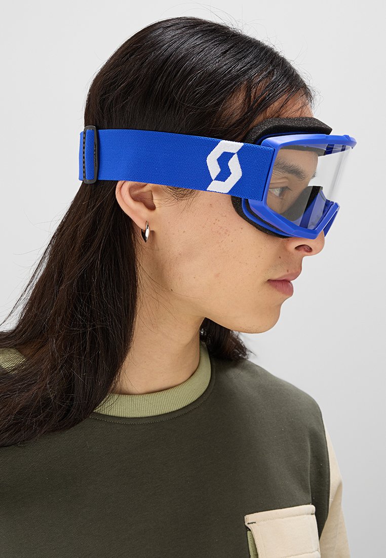 Blaue Sportbrille mit transparenten Gläsern, einem weichen Band mit weißen Logo-Details. Abgerundete Form für Komfort und Sichtbarkeit.