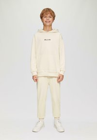 Cremfarbener Kapuzenpullover mit "SLVR"-Text, kombiniert mit passenden Sporthosen. Aus weichem Stoff gefertigt, mit einer lockeren Passform und gerippten Bündchen.