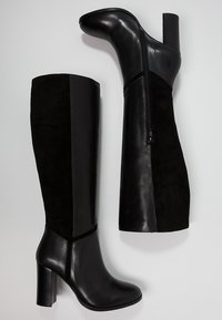 Botas negras hasta la rodilla con una combinación de cuero brillante y paneles de ante, con una cremallera lateral y un tacón alto y grueso.