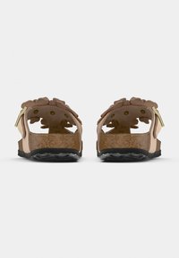 Οπίσθια όψη μπεζ σανδαλιών με ανοιχτά δάχτυλα, πάτους από φελλό, λουράκια με λουλουδάτα ανοίγματα και ρυθμιζόμενα κλείστρα σε χρυσό τόνο.