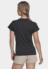 Camiseta negra de manga corta con cuello redondo, textura suave y costuras definidas, combinada con pantalones cortos beige claros.