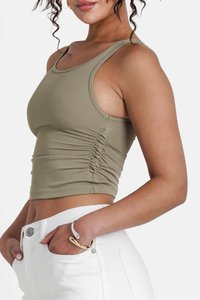 Olijfgroene cropped tanktop van ribstof met zijkanten met rimpeling. Draagt met hooggesneden witte jeans en een zilveren en gouden armband.