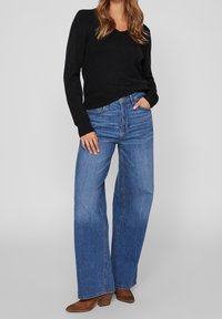 Svart långärmad v-ringad tröja i kombination med ljusblå högmidjade vida jeans och bruna klackiga ankelstövlar. Minimalistisk stil.