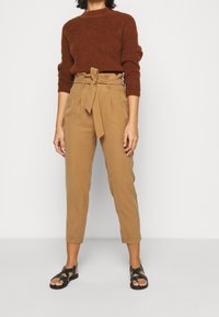 Brun stickad tröja med rund halsringning, kombinerad med högmidjade beiga byxor med knytbälte, kompletterad med svarta sandaler med nitar.